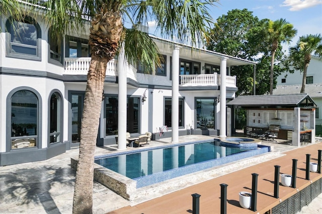 back of property featuring a pool with connected hot tub, a patio area, a balcony, and stucco siding