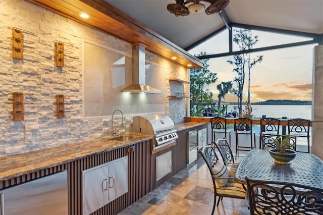 kitchen featuring lofted ceiling with beams, wall chimney exhaust hood, stone finish floor, and a sink