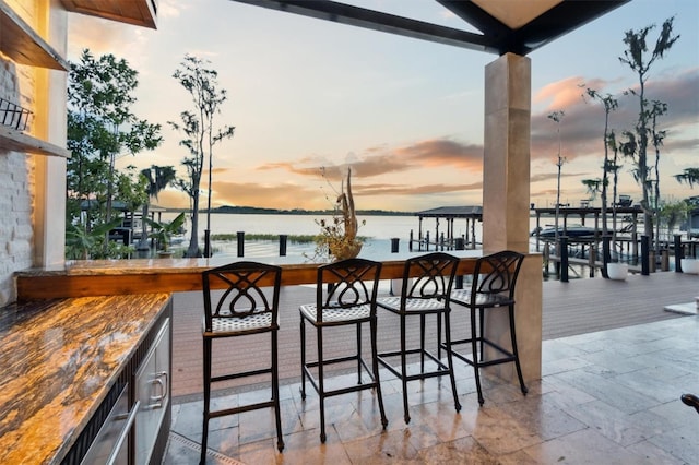 balcony at dusk featuring outdoor dry bar and a water view