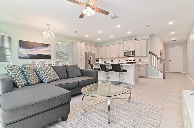 tiled living room with ceiling fan with notable chandelier