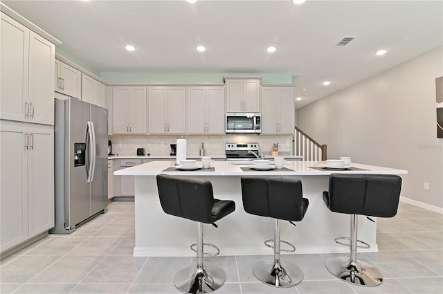 kitchen with white cabinetry, stainless steel appliances, an island with sink, a breakfast bar area, and tasteful backsplash