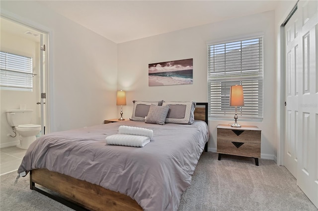 bedroom with a closet, ensuite bath, and light colored carpet