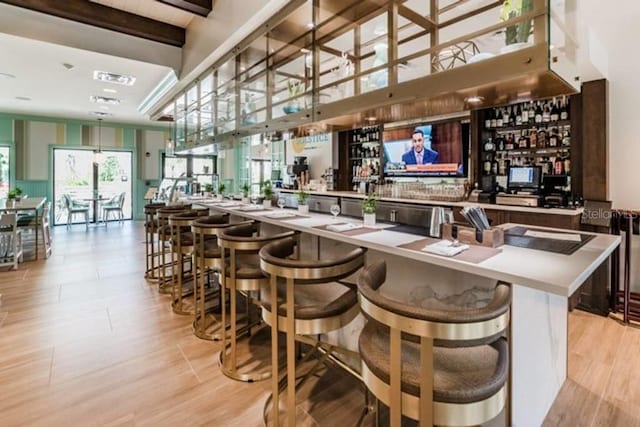 bar with beamed ceiling, a towering ceiling, and light hardwood / wood-style flooring