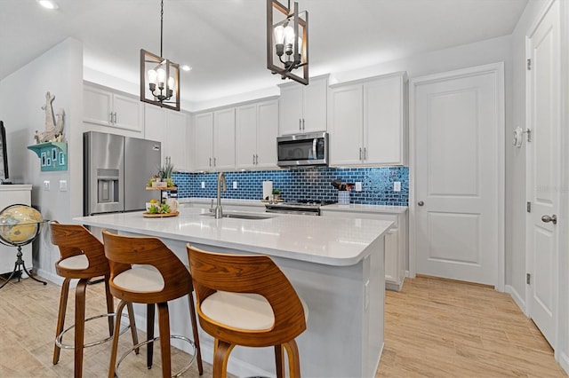 kitchen with appliances with stainless steel finishes, sink, hanging light fixtures, and a kitchen island with sink