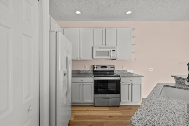 kitchen with white appliances, white cabinets, a textured ceiling, light hardwood / wood-style flooring, and light stone counters