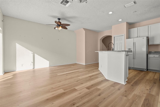 kitchen with a textured ceiling, white refrigerator with ice dispenser, a kitchen island with sink, and gray cabinets