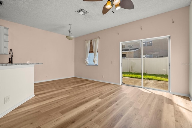 unfurnished living room featuring ceiling fan, sink, a textured ceiling, and light wood-type flooring