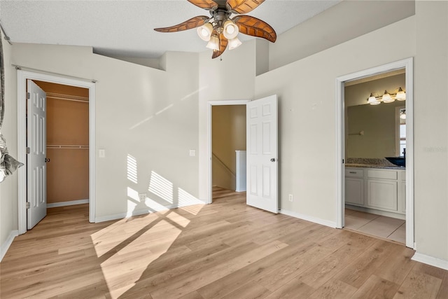 unfurnished bedroom with a spacious closet, light hardwood / wood-style floors, ceiling fan, ensuite bath, and a closet