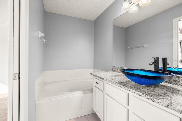 bathroom with vanity, tile patterned flooring, a textured ceiling, and tiled tub