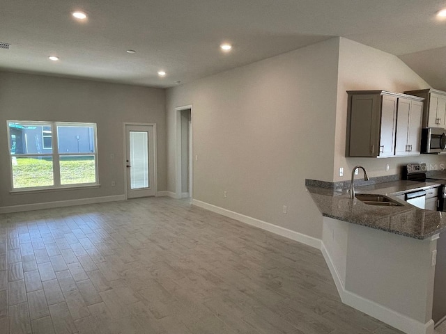 kitchen featuring kitchen peninsula, appliances with stainless steel finishes, dark stone counters, sink, and light hardwood / wood-style flooring