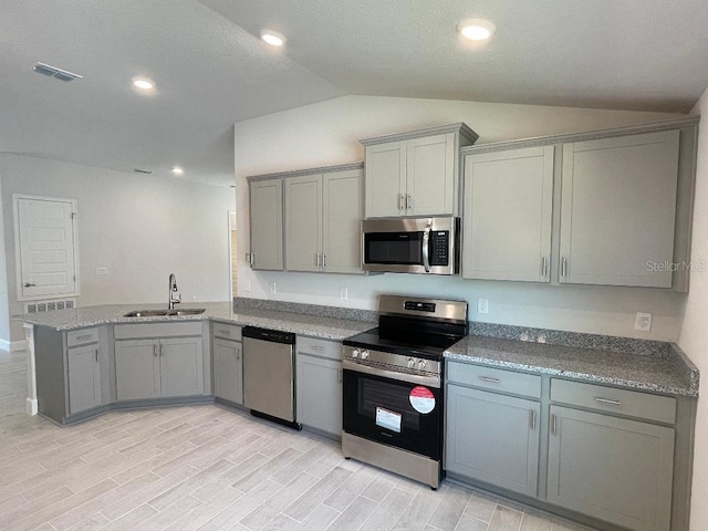 kitchen with lofted ceiling, sink, light wood-type flooring, kitchen peninsula, and stainless steel appliances