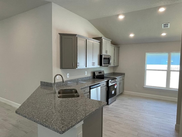 kitchen featuring lofted ceiling, sink, light hardwood / wood-style floors, kitchen peninsula, and stainless steel appliances