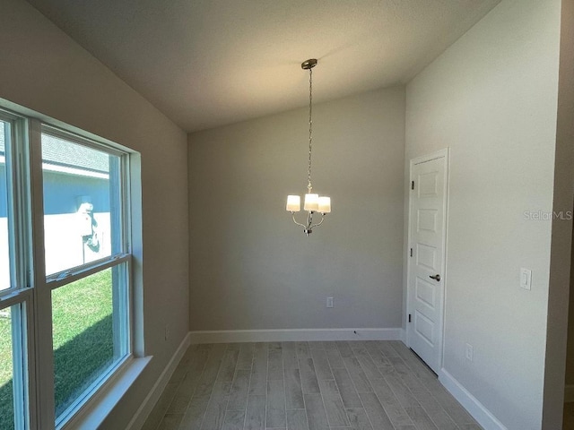 empty room with hardwood / wood-style floors, lofted ceiling, and a notable chandelier