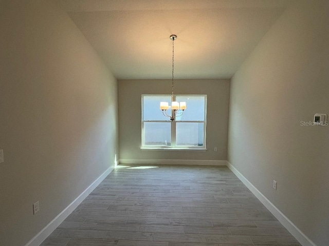 unfurnished dining area with hardwood / wood-style flooring, an inviting chandelier, and lofted ceiling