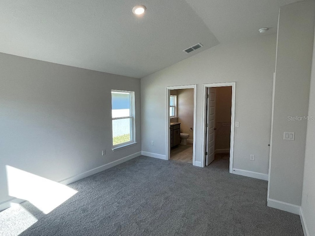 unfurnished bedroom featuring a spacious closet, dark colored carpet, ensuite bathroom, vaulted ceiling, and a closet