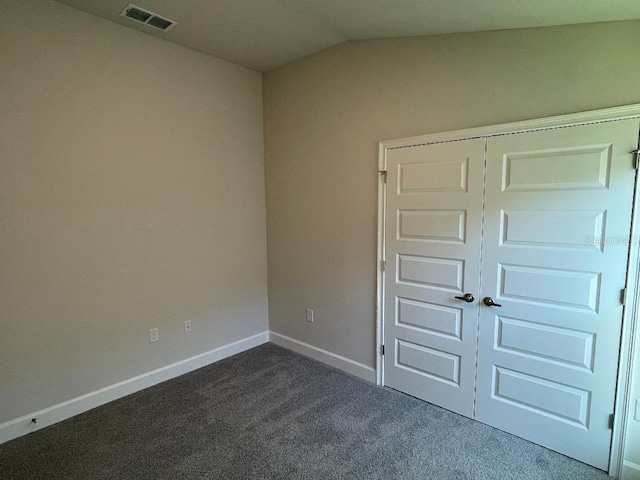 unfurnished bedroom featuring dark colored carpet, lofted ceiling, and a closet