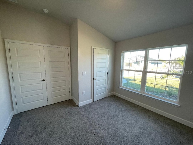 unfurnished bedroom with dark carpet, a closet, and lofted ceiling