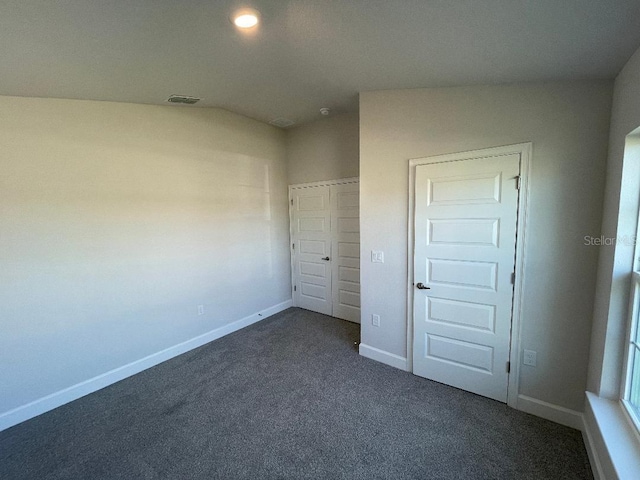 unfurnished bedroom featuring dark colored carpet, a closet, and lofted ceiling