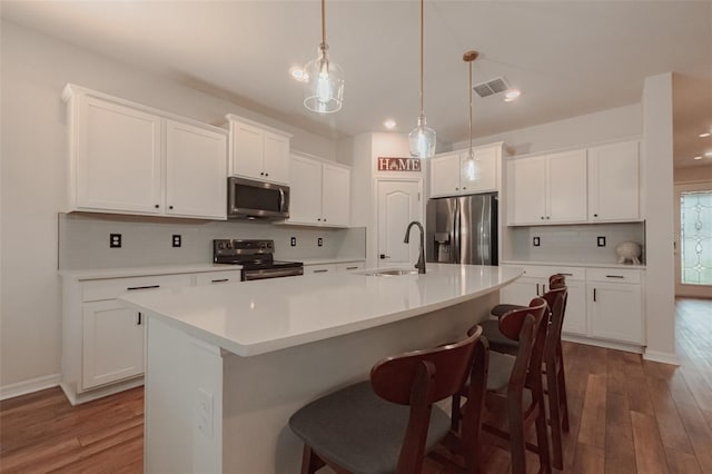 kitchen featuring a center island with sink, stainless steel appliances, decorative backsplash, pendant lighting, and white cabinets