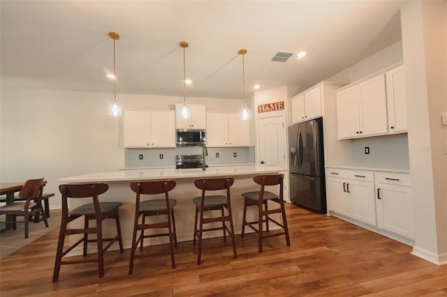 kitchen with an island with sink, pendant lighting, stainless steel appliances, and white cabinetry