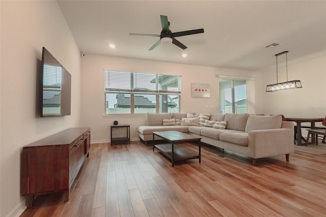 living room featuring ceiling fan with notable chandelier and light wood-type flooring