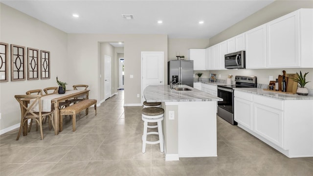 kitchen with light stone countertops, white cabinets, appliances with stainless steel finishes, an island with sink, and a breakfast bar area