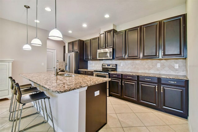 kitchen featuring a center island with sink, appliances with stainless steel finishes, backsplash, decorative light fixtures, and sink