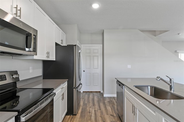 kitchen with wood-type flooring, white cabinets, sink, appliances with stainless steel finishes, and a textured ceiling