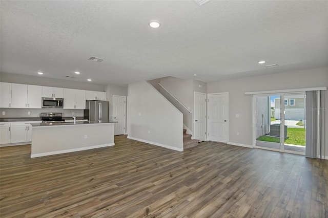 kitchen featuring appliances with stainless steel finishes, white cabinetry, a textured ceiling, a center island with sink, and dark hardwood / wood-style flooring