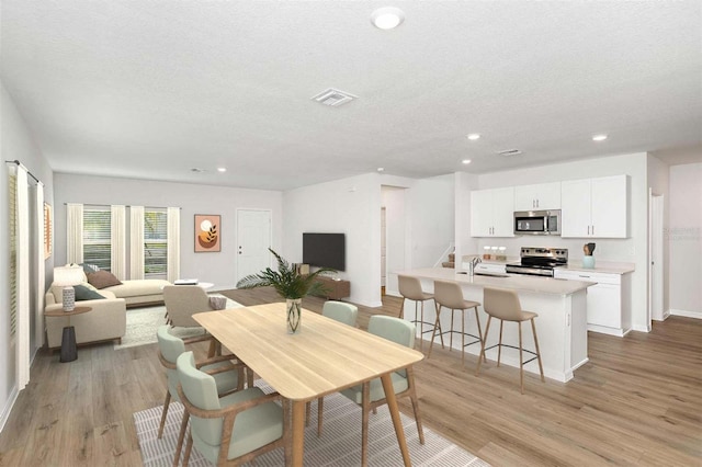 dining space featuring sink, light wood-type flooring, and a textured ceiling