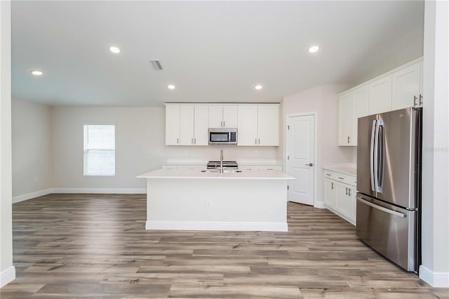 kitchen with white cabinets, light hardwood / wood-style flooring, stainless steel appliances, and a kitchen island with sink