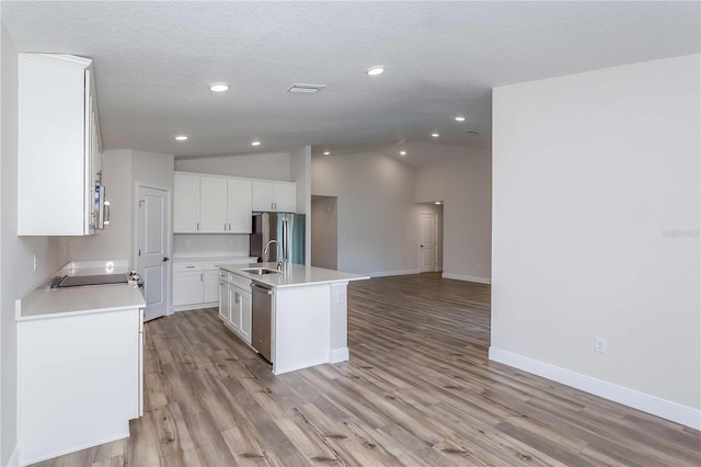 kitchen with a textured ceiling, lofted ceiling, white cabinetry, stainless steel appliances, and a kitchen island with sink