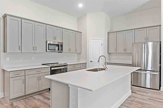 kitchen featuring light hardwood / wood-style flooring, appliances with stainless steel finishes, sink, gray cabinets, and an island with sink