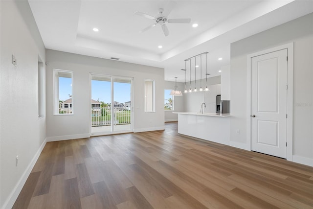 unfurnished living room featuring sink, hardwood / wood-style floors, a raised ceiling, and ceiling fan