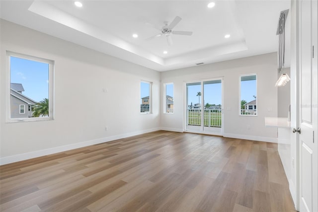 empty room with ceiling fan, light hardwood / wood-style floors, and a tray ceiling