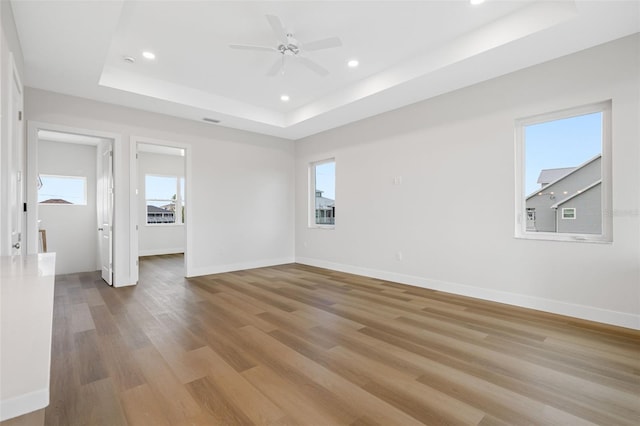 unfurnished room with a tray ceiling, light hardwood / wood-style flooring, ceiling fan, and plenty of natural light