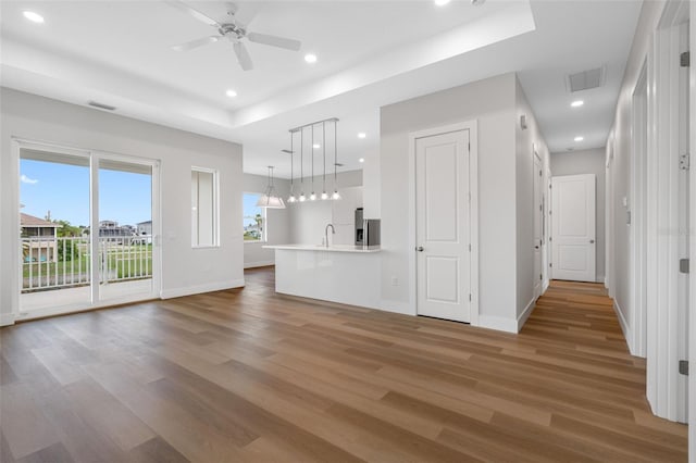 unfurnished living room with hardwood / wood-style flooring, ceiling fan, a raised ceiling, and sink