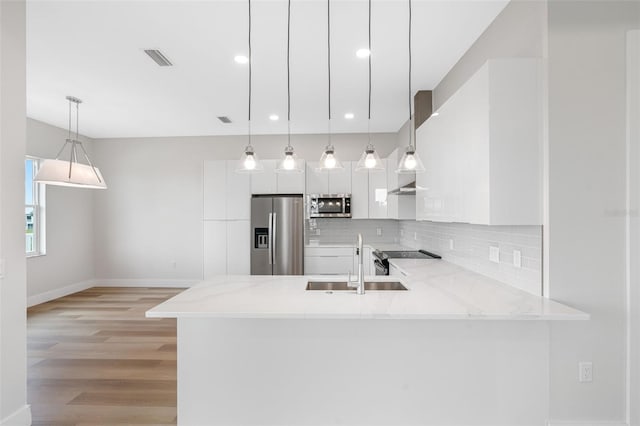 kitchen featuring hanging light fixtures, backsplash, stainless steel appliances, white cabinets, and kitchen peninsula