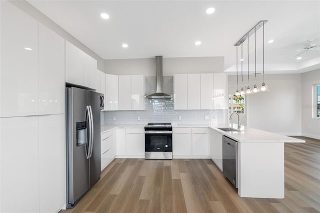 kitchen with wall chimney range hood, sink, stainless steel appliances, white cabinets, and decorative light fixtures