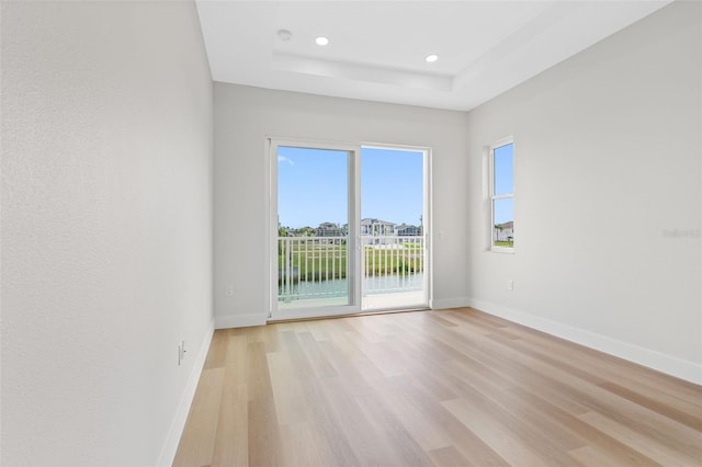 unfurnished room featuring a water view, a tray ceiling, and light hardwood / wood-style floors