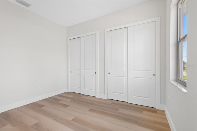 unfurnished bedroom with multiple closets and light hardwood / wood-style floors