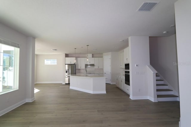 kitchen featuring sink, white cabinetry, decorative light fixtures, oven, and a kitchen island with sink