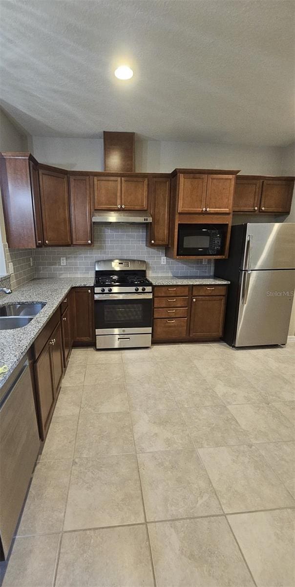 kitchen with light tile patterned floors, backsplash, light stone countertops, appliances with stainless steel finishes, and sink