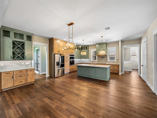 kitchen with dark hardwood / wood-style flooring, a kitchen island with sink, stainless steel appliances, decorative light fixtures, and sink