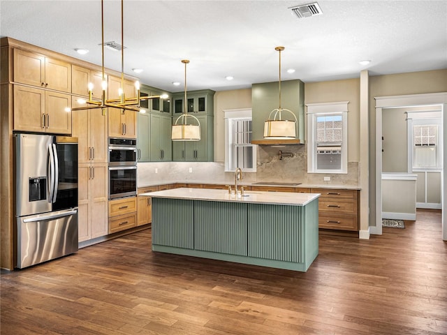 kitchen featuring dark wood-type flooring, decorative light fixtures, appliances with stainless steel finishes, and an island with sink