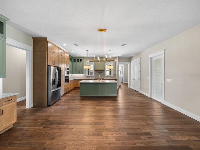 kitchen featuring hanging light fixtures, appliances with stainless steel finishes, dark hardwood / wood-style flooring, and a center island with sink