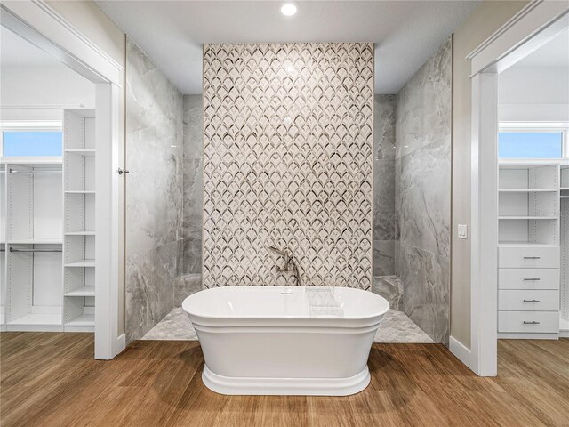 bathroom featuring plenty of natural light, wood-type flooring, tile walls, and a bathtub