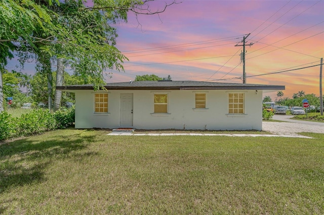 back of property at dusk featuring a lawn and stucco siding