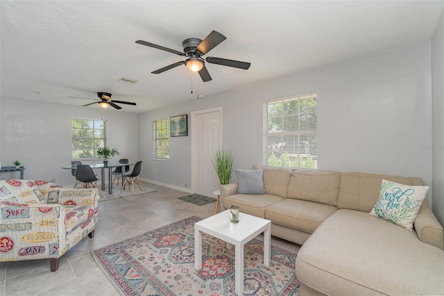 living room featuring visible vents, light tile patterned flooring, ceiling fan, a textured ceiling, and baseboards