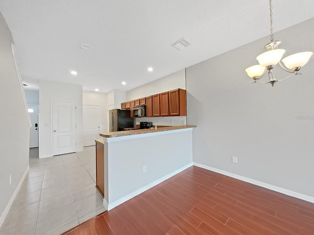 kitchen with pendant lighting, a notable chandelier, black appliances, light hardwood / wood-style floors, and kitchen peninsula